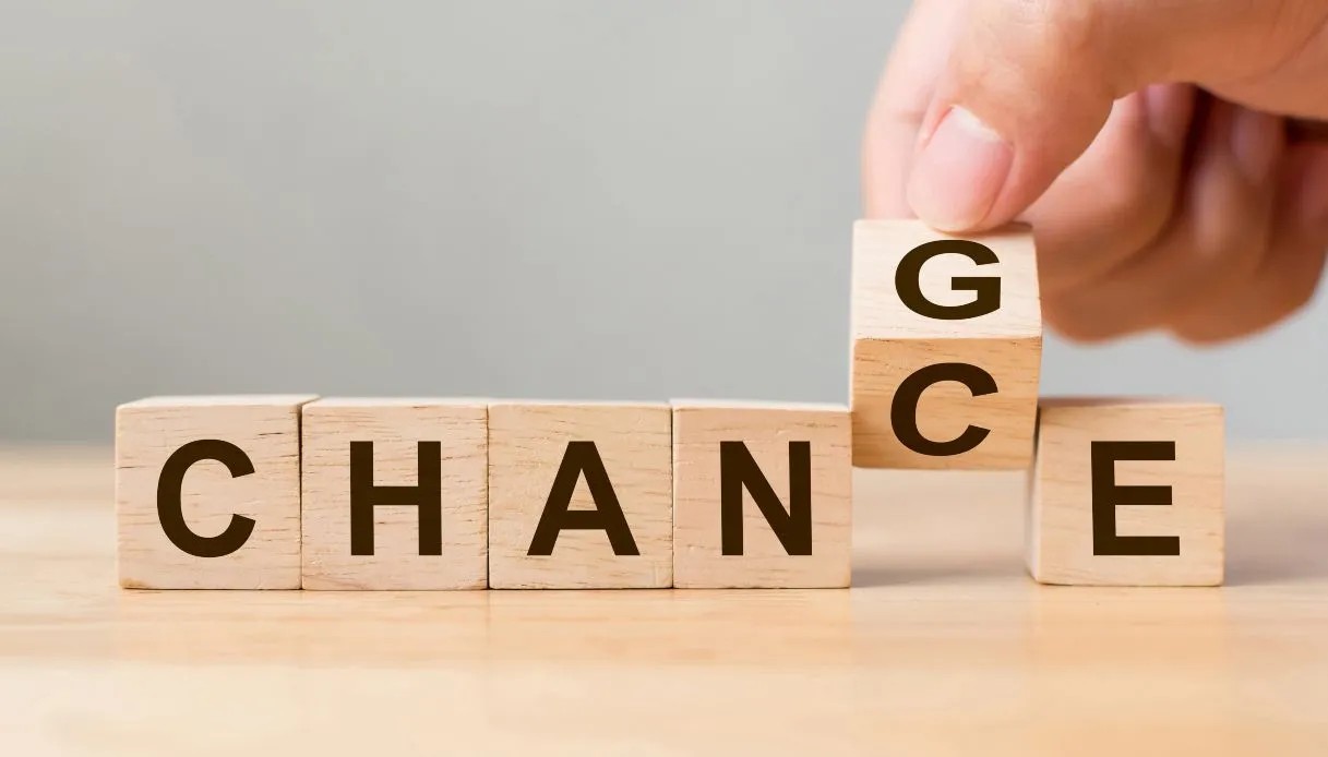 Wooden letter blocks that spell out "change" with a hand holding one piece
