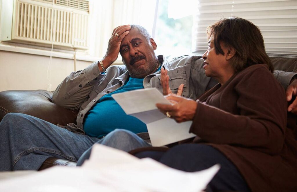 Older man and woman sitting on a couch looking at a paper bill